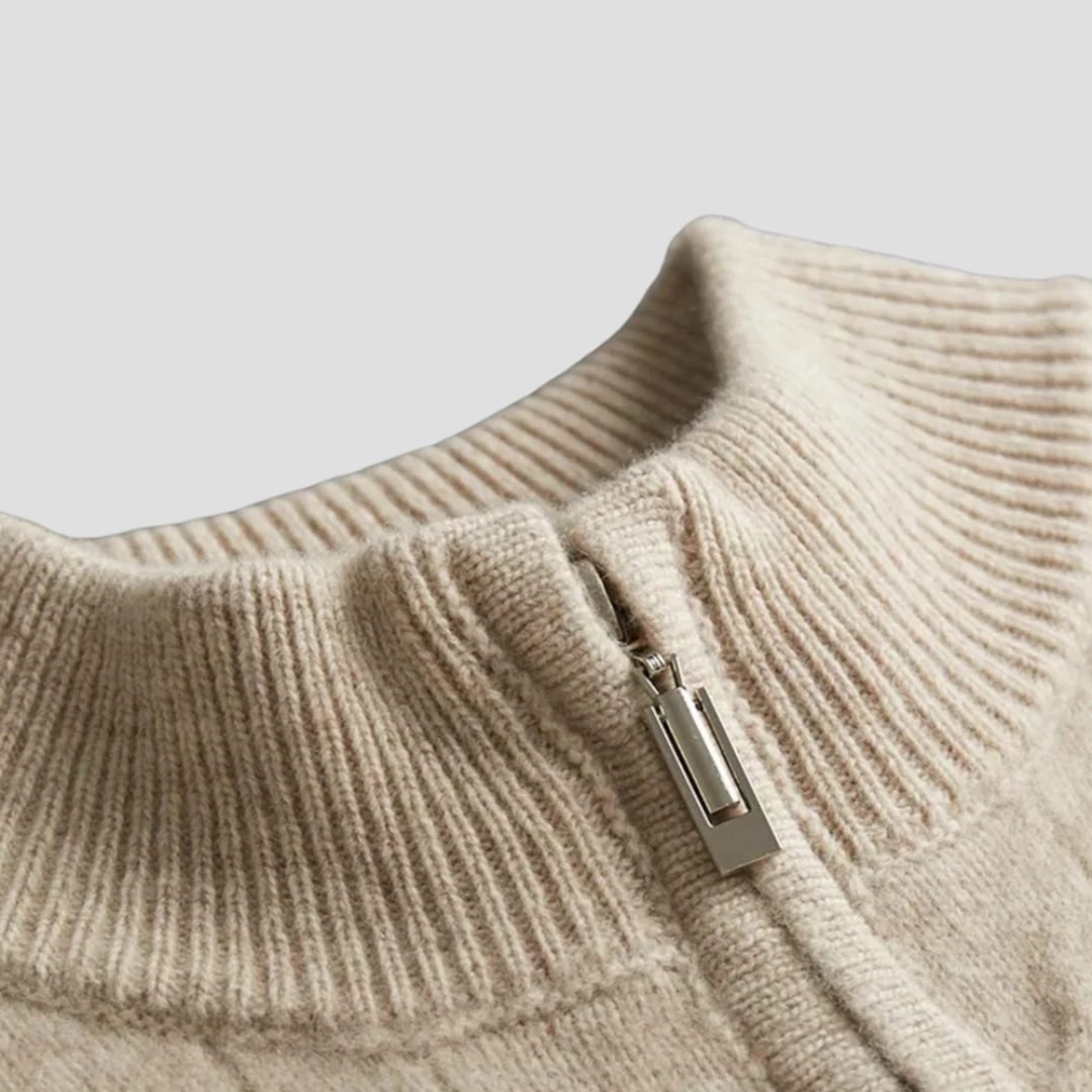 Beige kabelstrikket sweaterdetalje: halv lynlås ved høj krave og ribstrikket kant