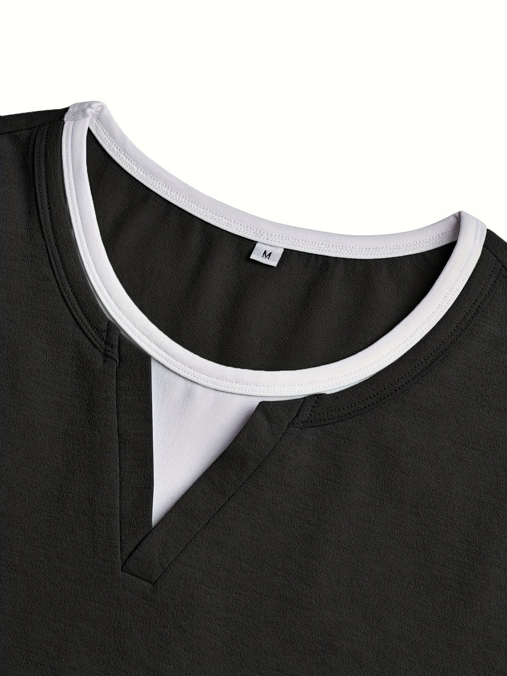 Detalje af sort henley-skjorte: V-udskæring og hvid kant samt halsudskæring.
