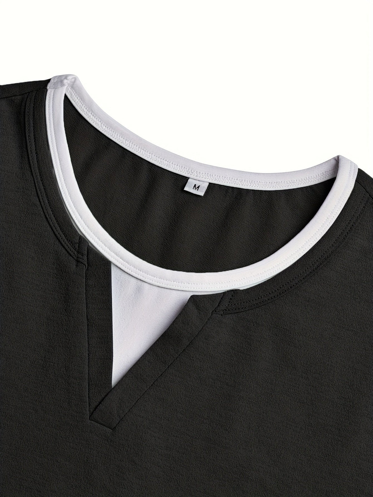 Detalje af sort henley-skjorte: V-udskæring og hvid kant samt halsudskæring.